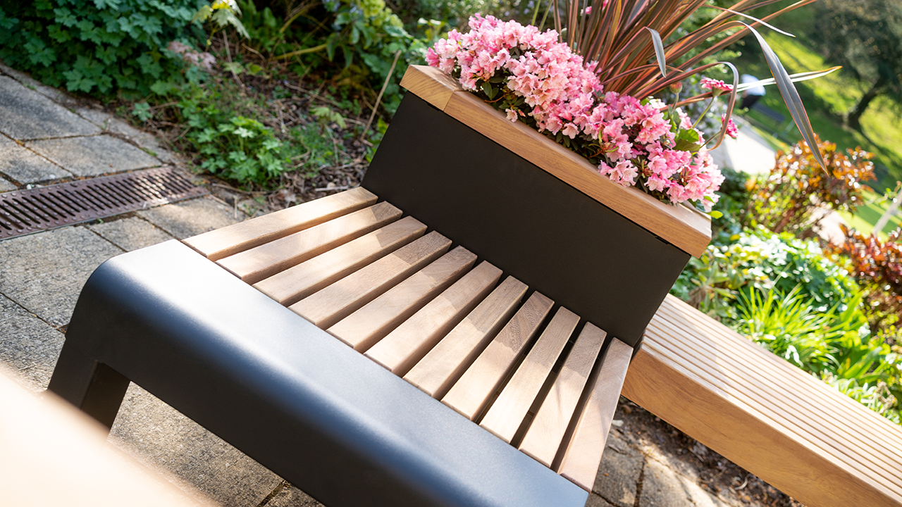 Close-up of a wooden bench and planter containing pink flowers.